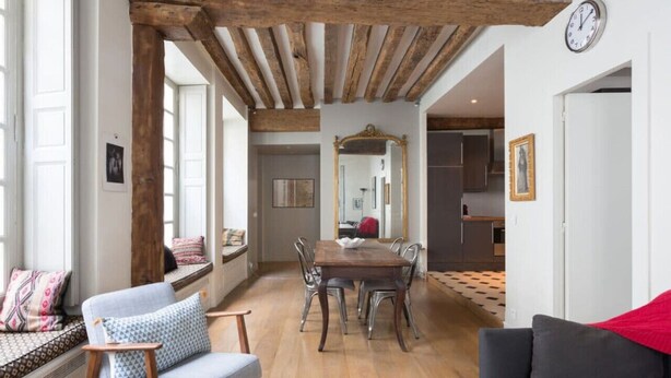 Un coin repas avec une table et des chaises en bois, un grand miroir au mur et une horloge.