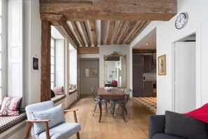 A dining area with a wooden table and chairs, a large mirror on the wall, and a clock. - Charming Appartment in Le Marais (Paris)
