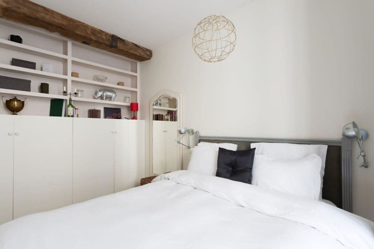 Une chambre bien rangée, avec un lit, une armoire blanche, des étagères contenant divers objets et un luminaire en forme de globe.