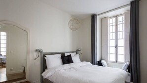 Une chambre à coucher avec un lit, un miroir, un lampadaire et une fenêtre avec des rideaux.