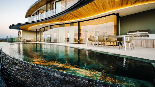 A modern house with a curved roof, a swimming pool, and a dining area with outdoor furniture. - Modern 6 BR Ocean View Villa with pingpong table, daily breakfast & cleaning (Playa Tamarindo)