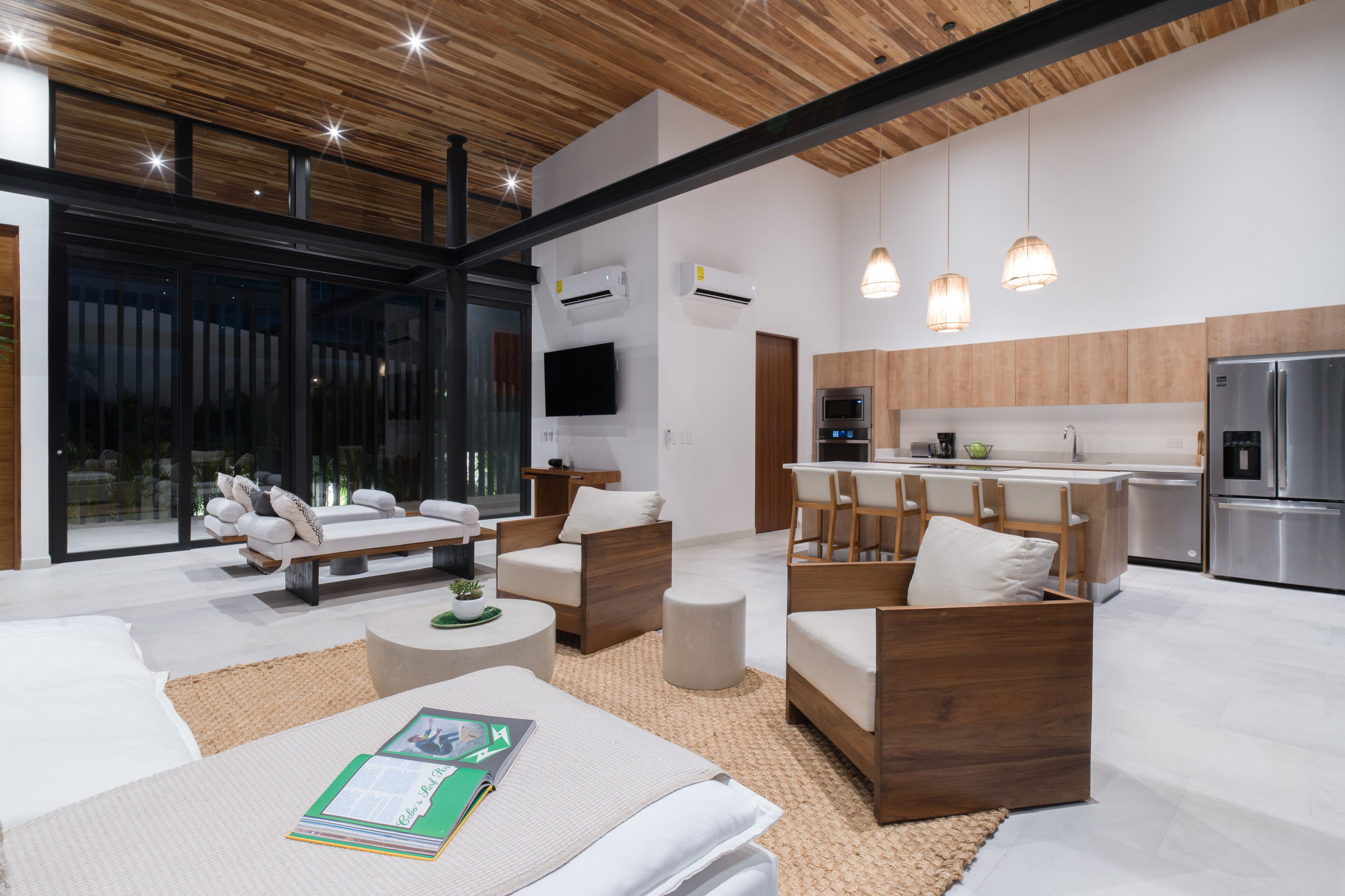 A modern living room with a sofa, chairs, and a coffee table. There is a kitchen area with a refrigerator, oven, and sink.