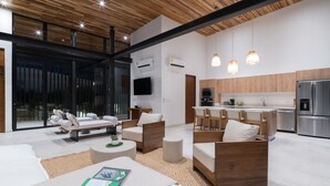 Un salon moderne comprenant un canapé, des fauteuils et une table basse. Il y a également un coin cuisine avec un réfrigérateur, un four et un évier.