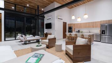 A modern living room with a sofa, chairs, and a coffee table. There is a kitchen area with a refrigerator, oven, and sink.