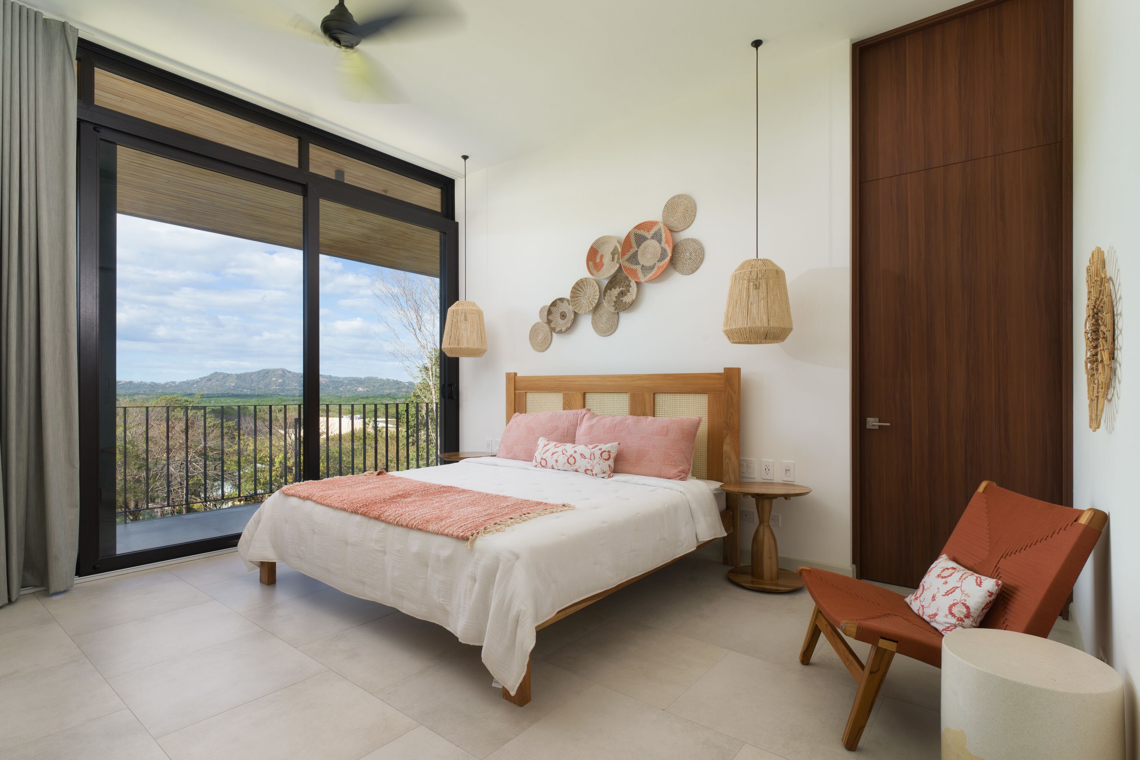 A bedroom with a large bed, a chair, a small table, and a view of the outdoors.