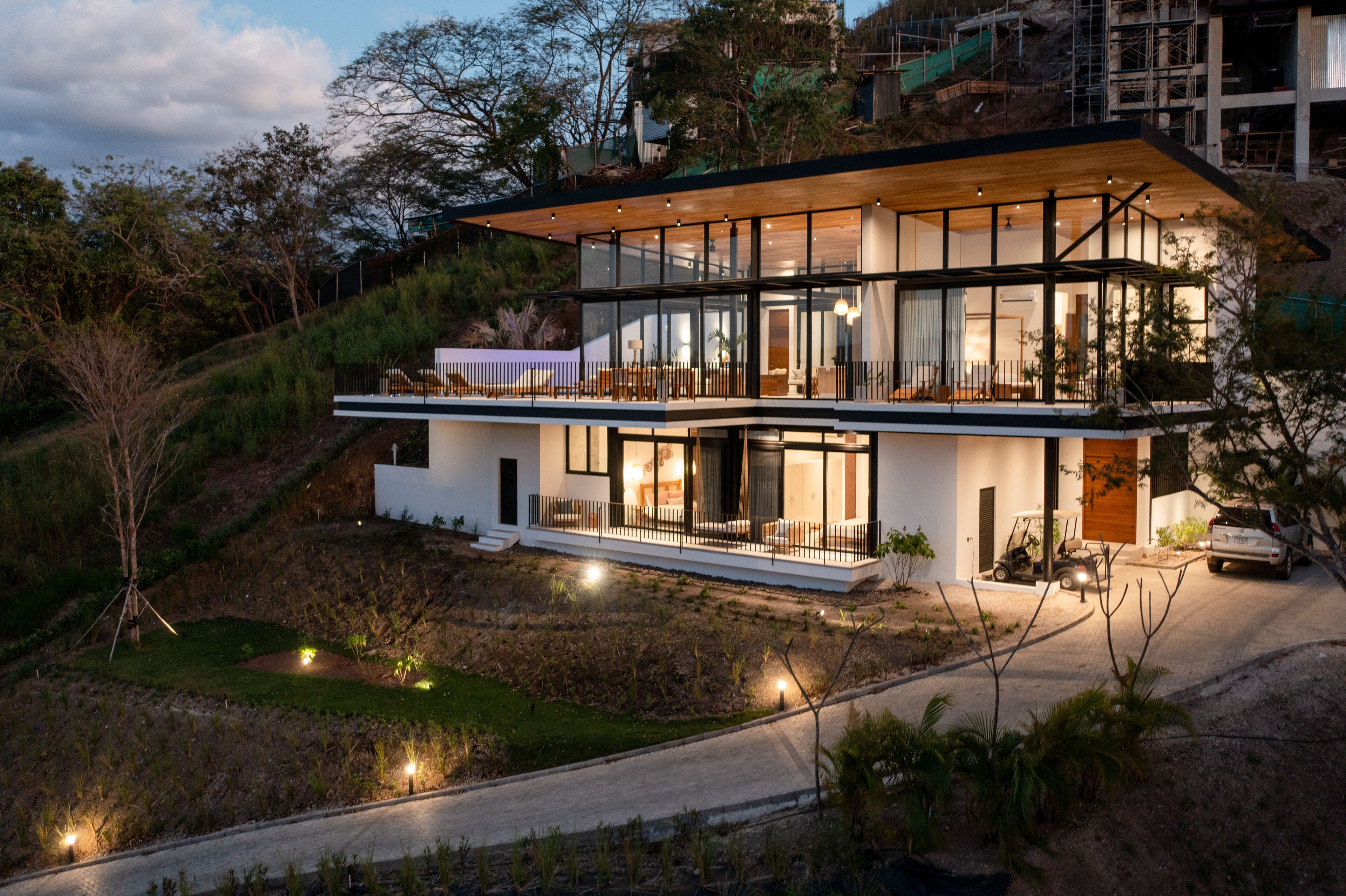 A modern two-story house with large glass windows, a wooden deck, and a driveway.