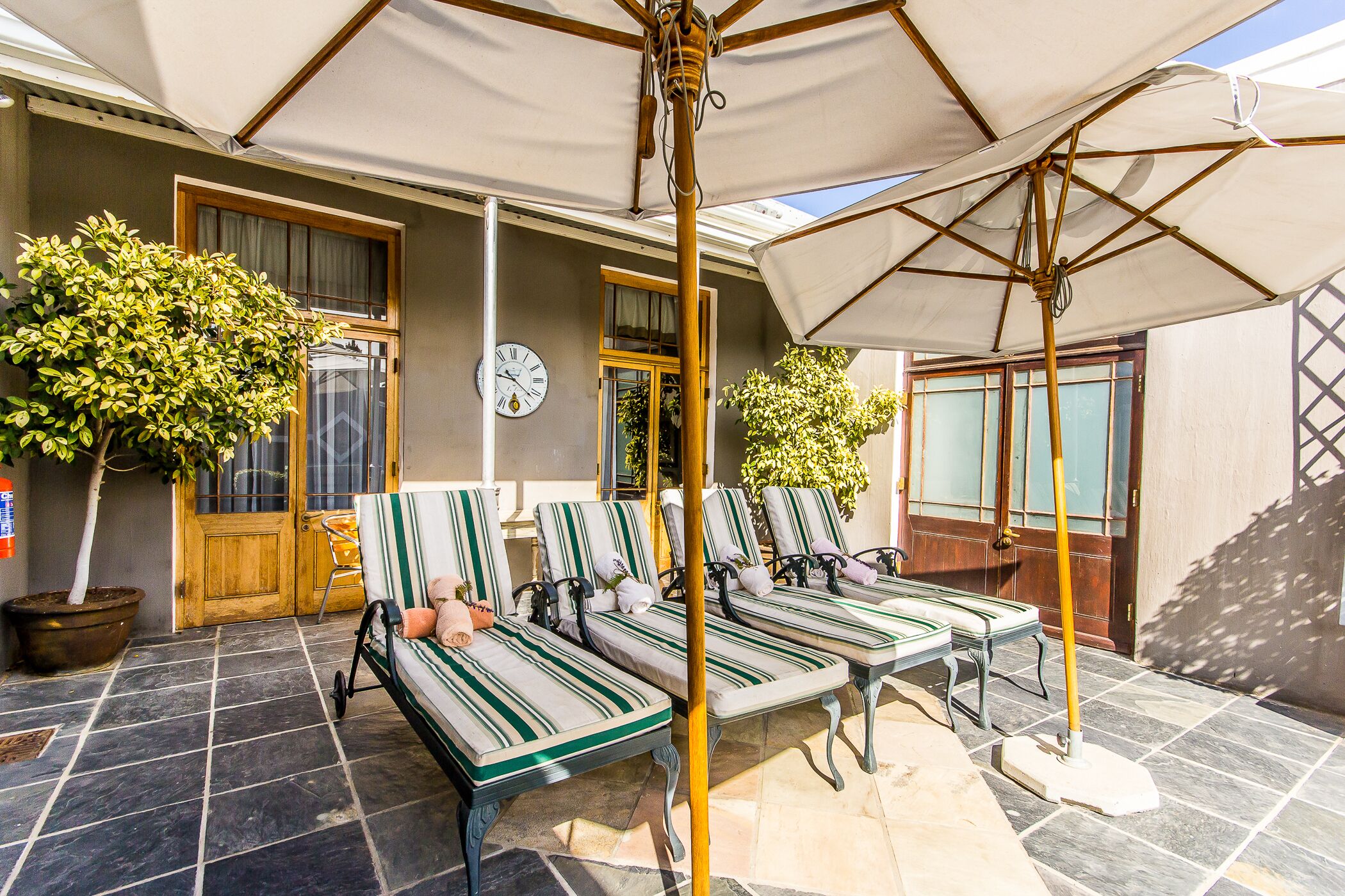 A covered outdoor seating area with striped lounge chairs and a large umbrella.