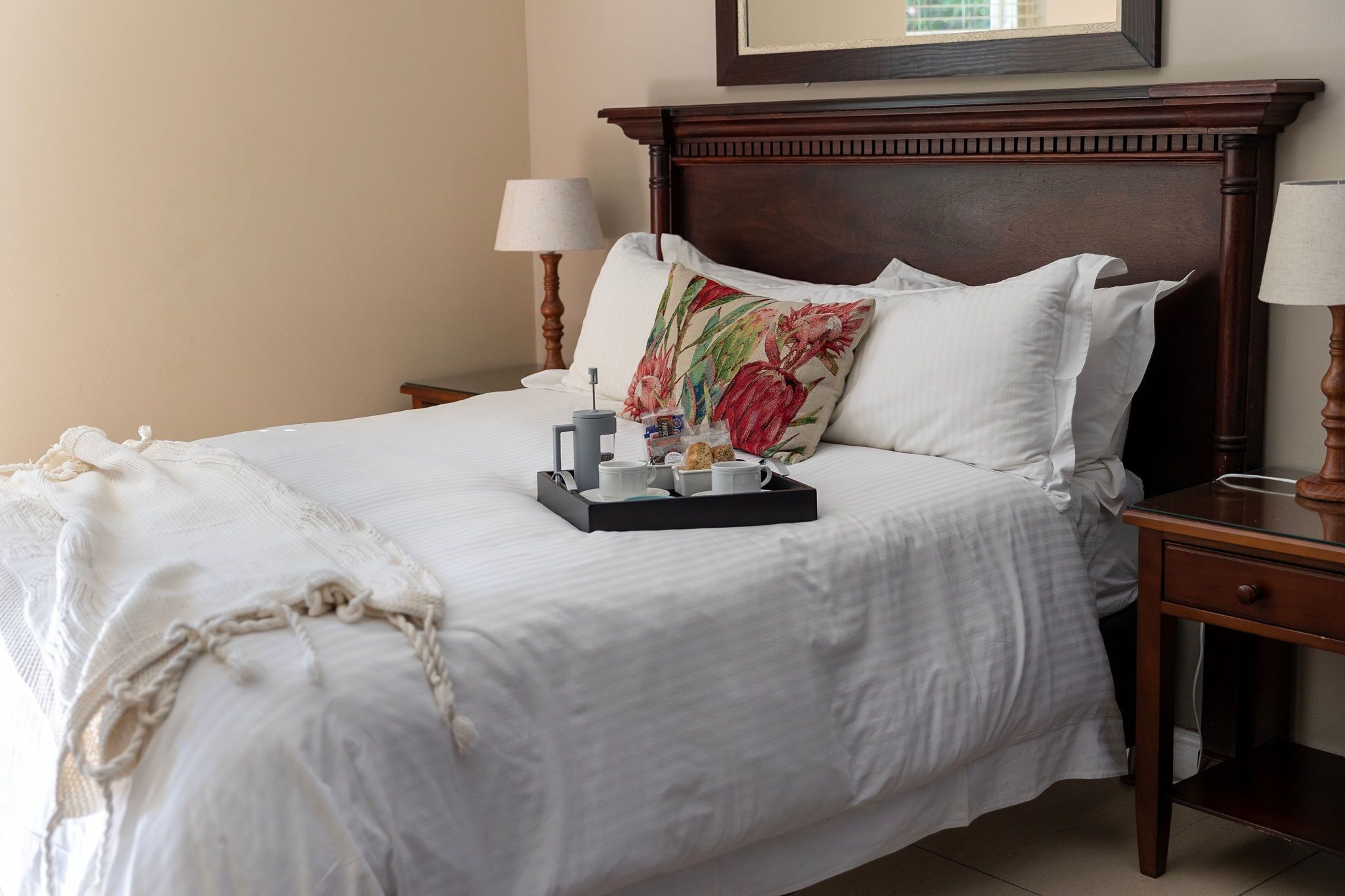 A neatly made bed with a tray of breakfast items, a floral pillow, and a wooden headboard.