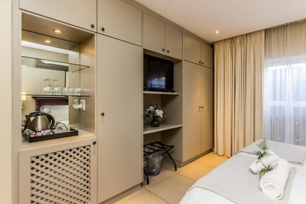 A hotel room with a bed, a TV, a minibar, a mirror, and a window with curtains.
