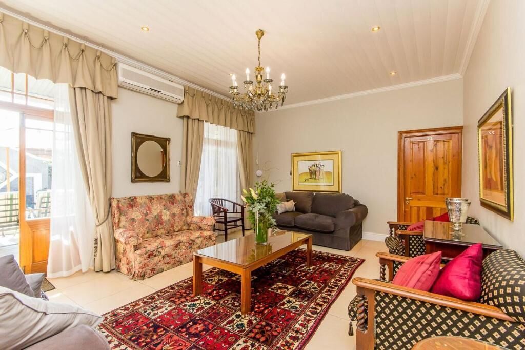 A well-lit living room with a chandelier, a floral sofa, a dark sofa, a patterned rug, and a wooden coffee table.