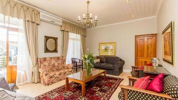 Un salón luminoso con candelabro, un sofá floral, un sofá oscuro, un tapete estampado y una mesa de centro de madera.