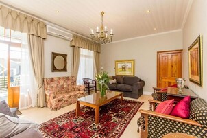 Un salón luminoso con candelabro, un sofá floral, un sofá oscuro, un tapete estampado y una mesa de centro de madera.