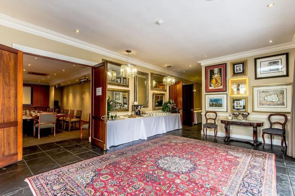 Une pièce spacieuse avec un grand tapis rouge à motifs, un coin repas avec une nappe blanche et un mur décoré de tableaux encadrés.