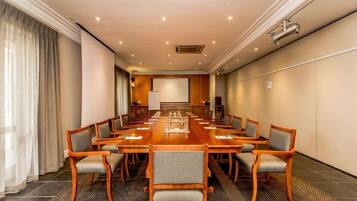 Un salón de conferencias con una larga mesa, varias sillas y una pantalla de proyector.