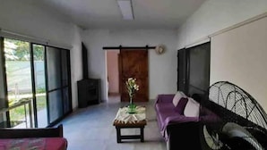 Un grand salon comprenant un canapé, une petite table avec un vase et un ventilateur.