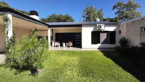 Une maison moderne dotée d’un patio couvert, d’un petit jardin et d’un climatiseur installé sur le toit.