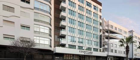 Un hotel moderno de varios pisos con un llamativo letrero de 'Courtyard by Marriott', grandes ventanales y un diseño limpio y contemporáneo.