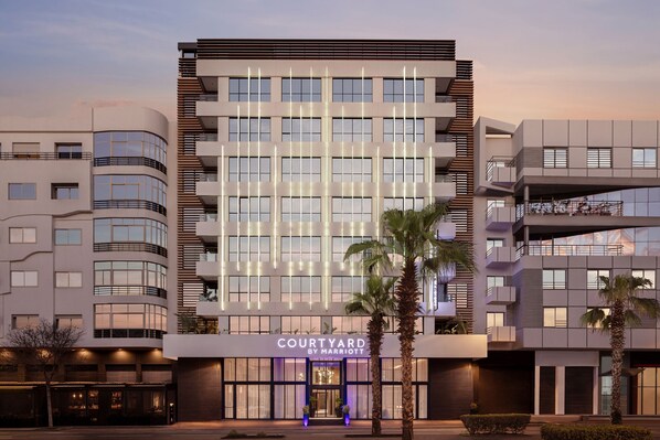 A modern hotel with a prominent 'Courtyard by Marriott' sign, featuring a multi-story structure with balconies and large windows.