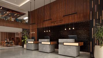 A modern hotel lobby with a wooden reception desk, a seating area, and a mezzanine level.