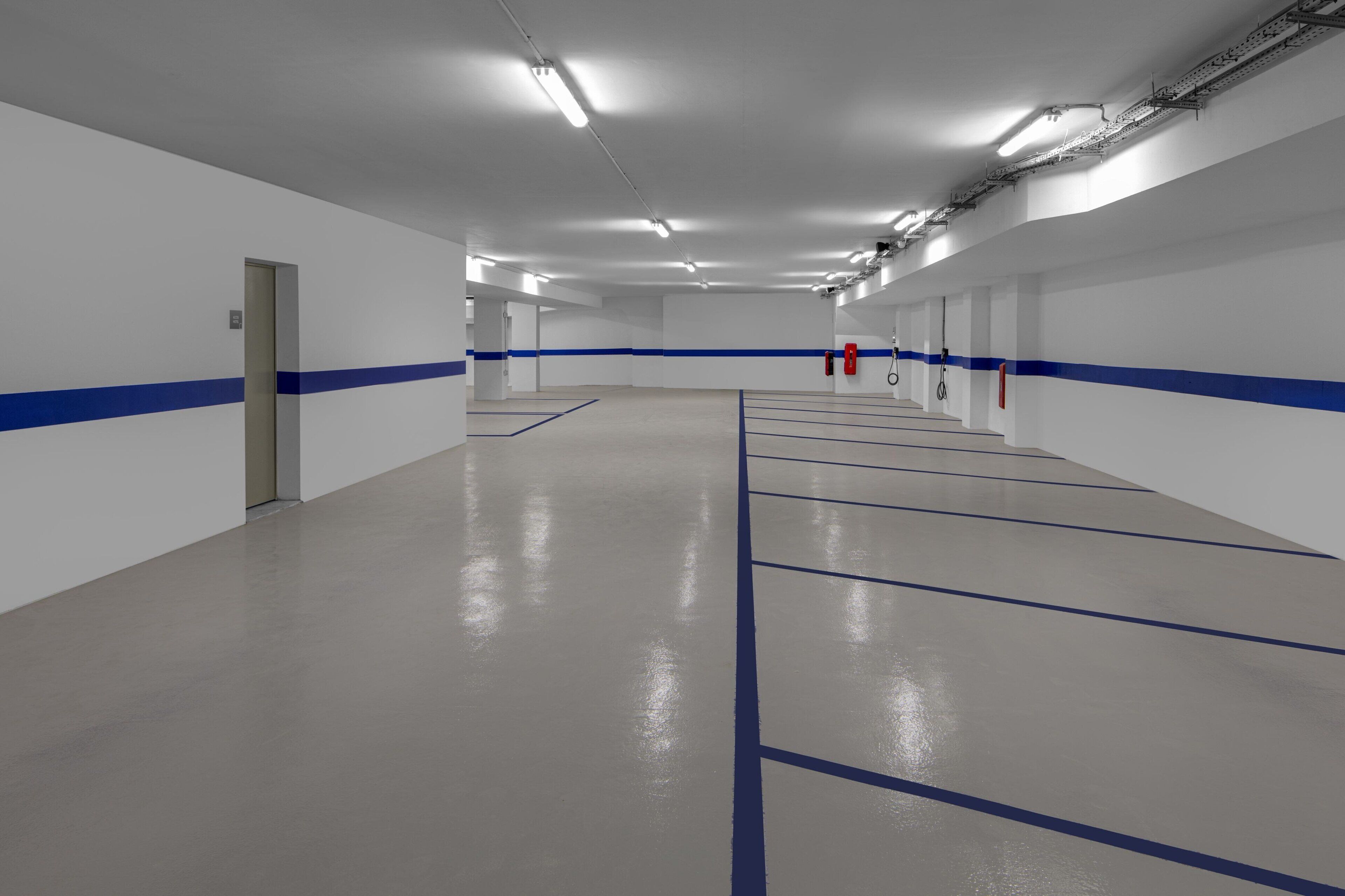 A spacious indoor parking area with clear lines marking parking spaces, a clean floor, and a blue stripe along the walls.