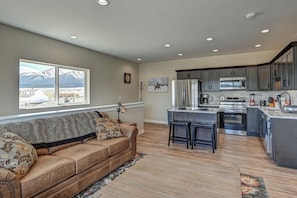 A modern kitchen with a large island, dark cabinetry, and a view of mountains through a window.