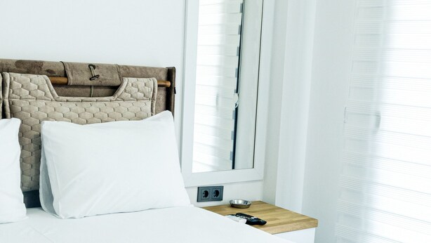 Habitación de hotel con una cama, una mesita de noche con un cuenco y un mando a distancia, y una ventana con persianas.