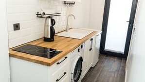 Cocina compacta con encimera de madera, estufa integrada, cafetera, lavabo y lavadora.