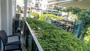 Un balcón con vistas a un área de restaurante, asientos al aire libre y vegetación.