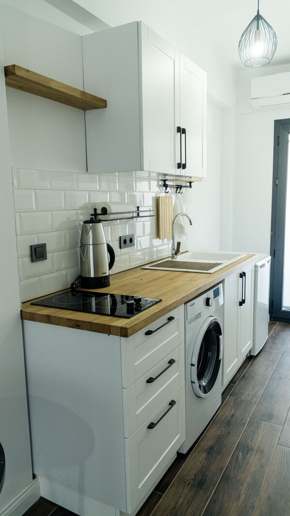 A compact kitchen with white cabinets, a wooden countertop, a built-in washing machine, and a hanging light fixture. - Port Marmaris Rooms (Marmaris)