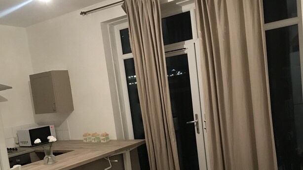 A modern hotel room with a kitchenette, a bed, a small wooden table, and a sliding glass door leading to a balcony. - Charming 3-bed Flat in London (London)