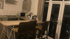 A modern kitchen with a central island, bar stools, a drying rack, and a view of the outside through a glass door. - Charming 3-bed Flat in London (London)