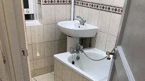 A bathroom with a white sink, a bathtub, and a toilet. The floor is tiled with large square tiles. - Charming 3-bed Flat in London (London)