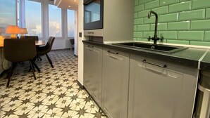 A modern kitchen with grey cabinets, a black countertop, and a green tiled backsplash. There is a window with a view of the city, and a dining area with a table and chairs. - Casa Anna (La Puntilla)