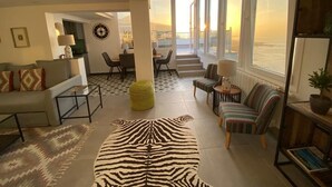 A spacious living room with a large zebra-patterned rug, a sofa, a dining area, and a view of the sea through large windows. - Casa Anna (La Puntilla)