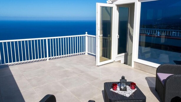 A balcony with a clear view of the ocean, a glass door, and a small table with a lantern and a red cup. - Casa Anna (La Puntilla)