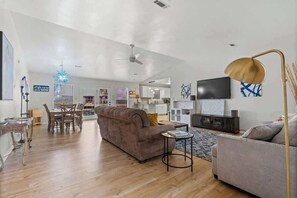 A spacious living area with a sofa, a coffee table, a TV, and a dining area with chairs and a table.