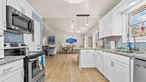 A modern kitchen with white cabinetry, stainless steel appliances, a dining area with a table and chairs, and a blue decorative wall.