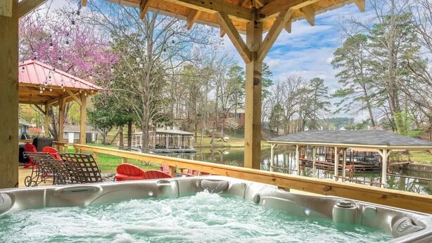 A hot tub with a wooden deck and a view of a lake and trees.