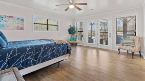 A bedroom with a bed, a ceiling fan, a window with blinds, a chair, and a plant.