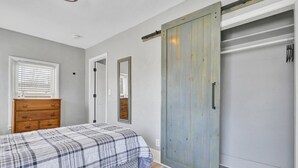 Un dormitorio con cama, cómoda, puerta corredera y espejo.