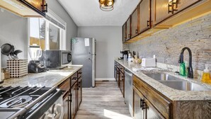 Una cocina con encimeras de granito, armarios de madera, estufa integrada, refrigerador y ventana que proporciona luz natural.