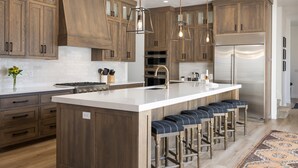 Une cuisine moderne avec des meubles en bois, un îlot central doté de tabourets de bar, des appareils en acier inoxydable et un éclairage suspendu.