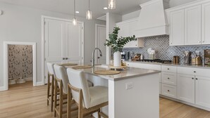 A modern kitchen with white cabinetry, a central island with bar stools, pendant lighting, and a backsplash with a geometric pattern.
