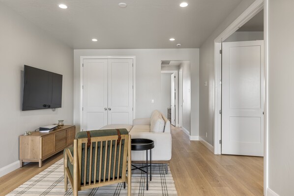 A modern living room with a flat-screen TV, a wooden cabinet, a green chair, a white sofa, and a plaid rug.