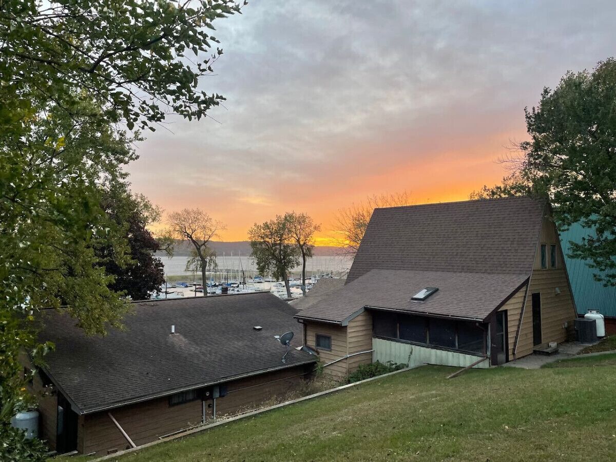 Ein Haus mit geneigtem Dach, einer Satellitenschüssel und Blick auf ein Gewässer im Sonnenuntergang.
