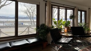 Amplia habitación con ventanas grandes, un sofá de cuero negro, un banco de madera y varias plantas en macetas.