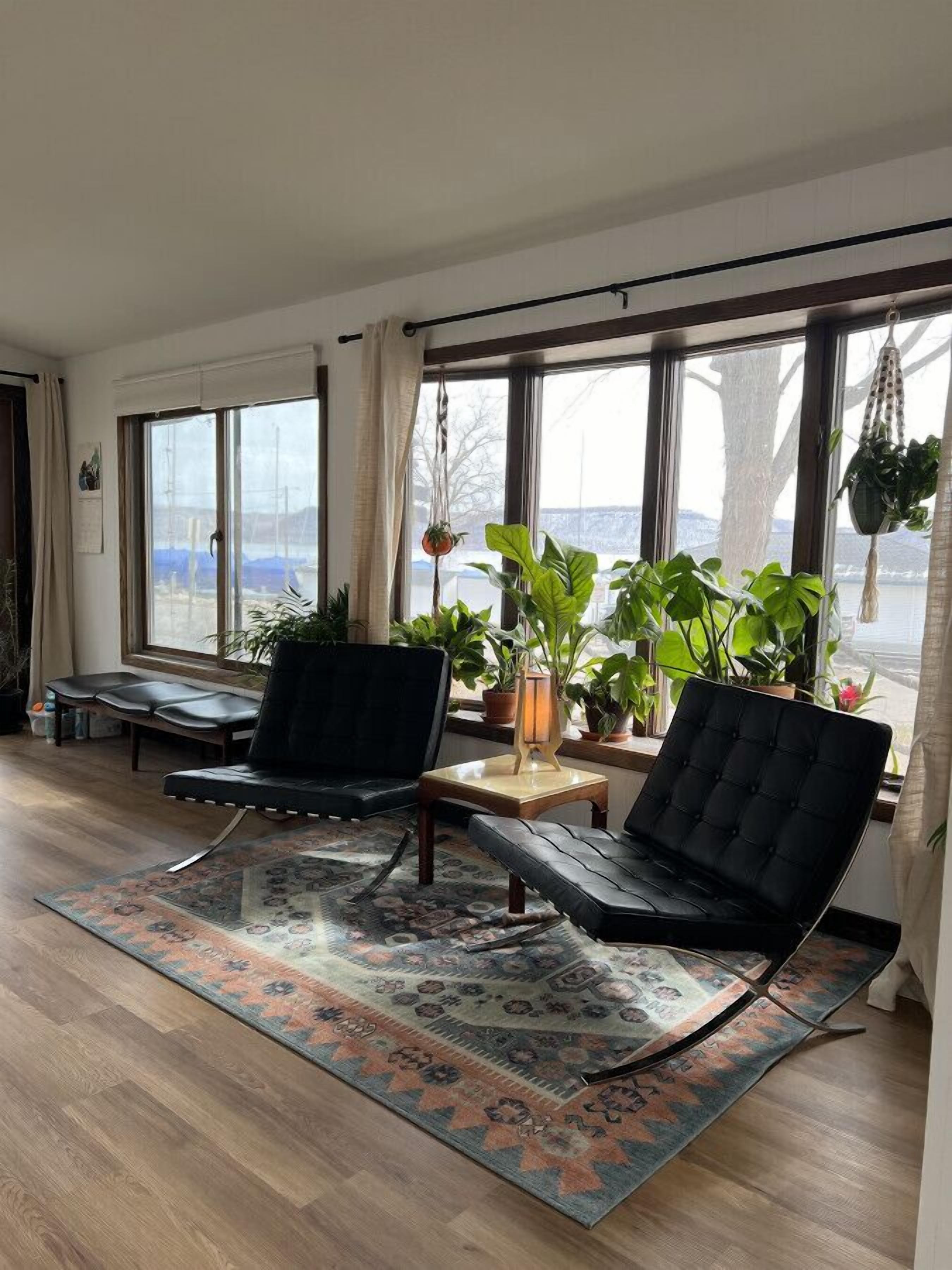 A spacious living room with large windows, a black leather sofa, a wooden coffee table, and a patterned rug.