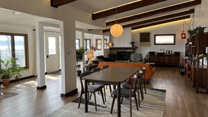 Un salón espacioso con una gran mesa de comedor de madera, asientos cómodos, una chimenea y vistas al exterior.