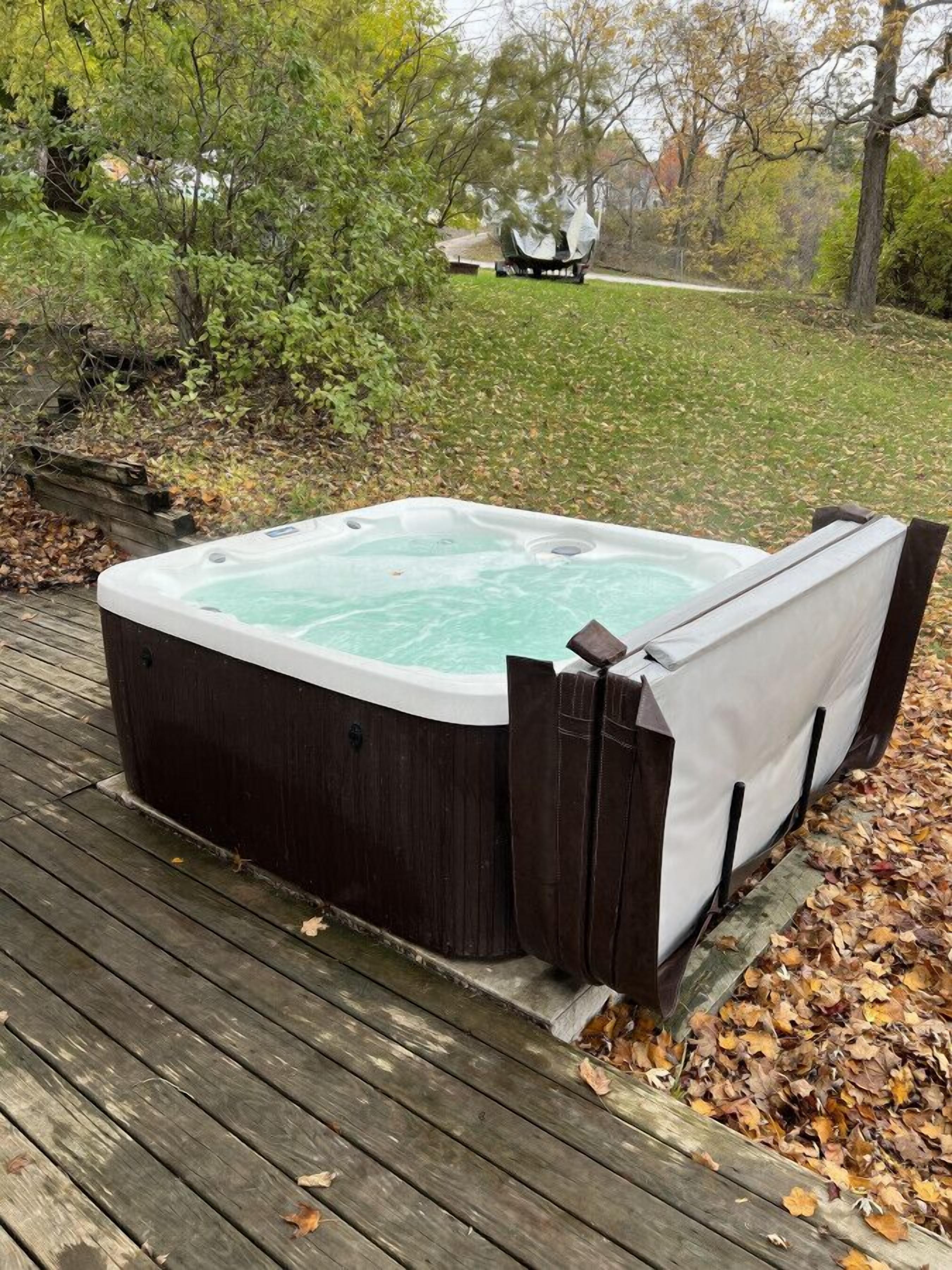 A hot tub on a wooden deck surrounded by trees and a grassy area.