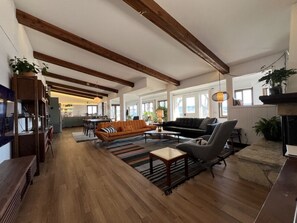 A spacious living area with wooden floors, a sofa, a chair, and a coffee table. There is a kitchen in the background with a dining table and chairs. - Waterfront Bungalow + Hot Tub • Marina, Lake Pepin (Pepin)